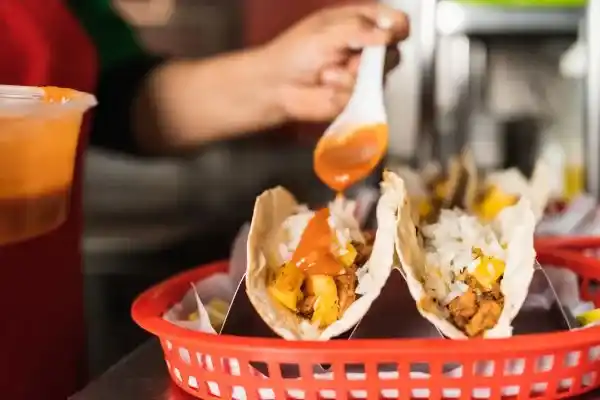 worker-pouring-sauce-on-tacos-in-a-basket-to-serve
